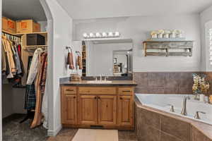 Full bathroom featuring vanity, a garden tub, a walk in closet, and dark tile patterned flooring