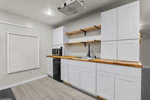 Kitchen with wood counters, open shelves, white cabinetry, a textured ceiling, and dishwasher