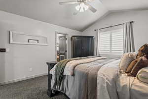 Bedroom featuring vaulted ceiling, dark carpet, ensuite bathroom, and ceiling fan