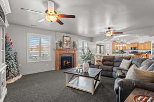 Living area featuring a ceiling fan, a tiled fireplace, dark carpet, a textured ceiling, and lofted ceiling