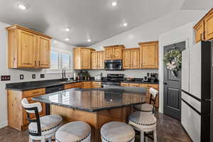Kitchen with a breakfast bar, freestanding refrigerator, lofted ceiling, black electric range oven, and a kitchen island