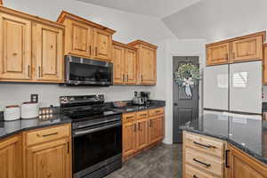 Kitchen with stainless steel appliances, dark stone counters, vaulted ceiling, and dark tile patterned floors