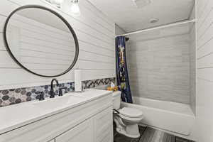 Bathroom with vanity, shower / bath combination with curtain, wooden walls, dark tile patterned flooring, and backsplash