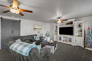 Living room featuring a ceiling fan, a barn door, and carpet flooring