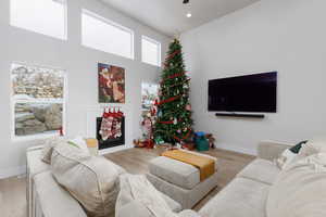 Living area with a fireplace, light wood-style flooring, a high ceiling, recessed lighting, and a ceiling fan