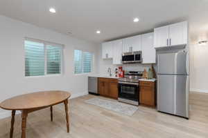 Kitchen featuring appliances with stainless steel finishes, white cabinetry, brown cabinetry, light wood-style flooring, and recessed lighting