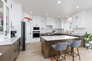 Kitchen featuring glass insert cabinets, light stone counters, a kitchen bar, a kitchen island, and light wood-style floors