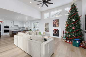 Living area featuring a towering ceiling, light wood-style floors, a ceiling fan, and recessed lighting