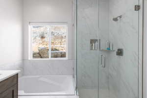 Full bath with vanity, a bath, and a marble finish shower