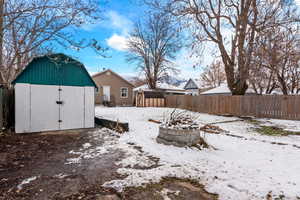 Snowy yard with a shed, a fenced backyard, and a fire pit