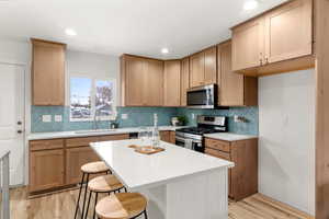 Kitchen with a breakfast bar area, stainless steel appliances, light stone countertops, a center island, and decorative backsplash