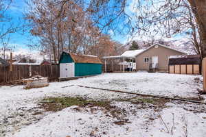 Yard covered in snow with a fenced backyard, a storage shed, a patio, and a carport