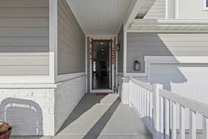 Doorway to property featuring a porch, brick siding, and a garage