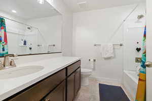 Guest bathroom with shower / bathtub combination with curtain, vanity, and light tile patterned flooring