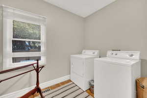Washroom with light wood-type flooring and washing machine and clothes dryer
