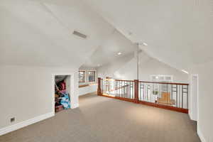 Additional living space loft with a textured ceiling, vaulted ceiling, and carpet flooring