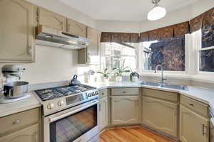 Kitchen with stainless steel gas range, light countertops, under cabinet range hood, and light wood-type flooring