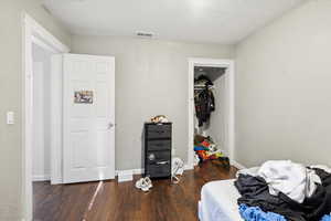 Bedroom with a textured ceiling, dark wood finished floors, a textured wall, and a closet