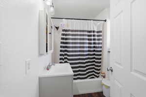 Bathroom with shower / bath combination with curtain, vanity, dark wood-style floors, and a textured wall
