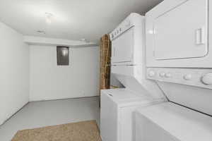 Laundry area featuring concrete floors, stacked washer / dryer, electric panel, brick wall, and a textured ceiling