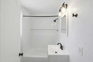 Bathroom featuring a textured wall, vanity, and shower / bath combination
