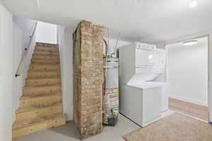 Laundry area with stacked washing machine and dryer, strapped water heater, finished concrete floors, and a textured ceiling