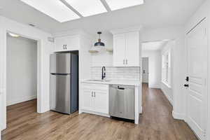 Kitchen with appliances with stainless steel finishes, white cabinets, backsplash, open shelves, and light wood-style flooring