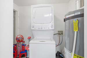 Laundry area featuring strapped water heater and stacked washer / dryer