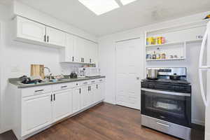 Kitchen featuring white appliances, white cabinets, dark wood finished floors, open shelves, and dark countertops