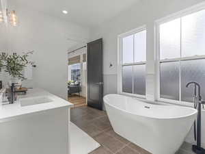 Full bath with a freestanding bath, wainscoting, double vanity, dark tile patterned flooring, and recessed lighting