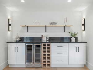 Indoor dry bar with open shelves, white cabinetry, wine cooler, dark stone countertops, and recessed lighting