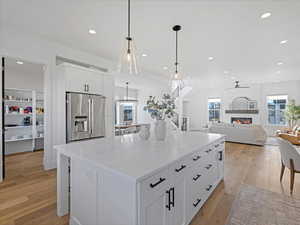 Kitchen with white cabinetry, light stone countertops, light wood-style floors, a center island, and high end fridge