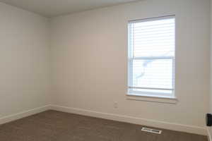 Empty room featuring baseboards and dark colored carpet