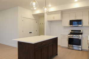 Kitchen featuring appliances with stainless steel finishes, dark brown cabinetry, decorative backsplash, a center island, and white cabinetry