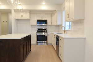 Kitchen with appliances with stainless steel finishes, white cabinets, decorative light fixtures, a kitchen island, and recessed lighting