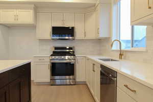 Kitchen featuring stainless steel appliances, dark brown cabinetry, white cabinets, decorative backsplash, and light stone counters
