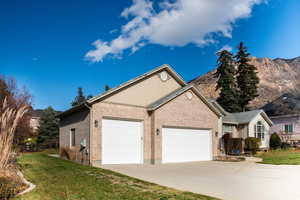 View of side of home featuring a yard, brick siding, a garage, driveway, and a mountain view