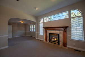 Unfurnished living room with carpet floors, arched walkways, and a tile fireplace