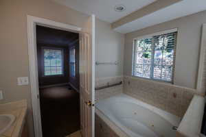 Bathroom with a tub with jets, vanity, and carpet floors