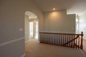 Hallway with vaulted ceiling, arched walkways, light carpet, and recessed lighting