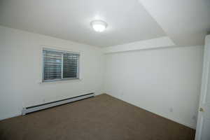 Carpeted empty room featuring a baseboard heating unit and baseboards