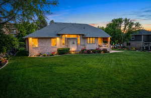 Back of house at dusk with a lawn, a shingled roof, and brick siding