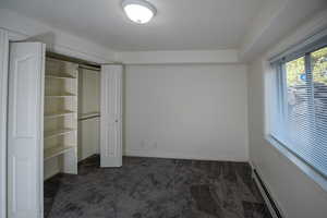 Unfurnished bedroom featuring a baseboard heating unit, a closet, and dark carpet
