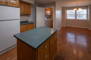 Kitchen featuring freestanding refrigerator, brown cabinets, dark wood finished floors, washing machine and dryer, and dark countertops