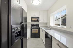 Kitchen with black appliances, white cabinets, light stone countertops, and a textured ceiling