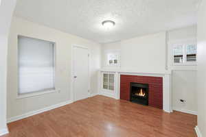 Unfurnished living room featuring a brick fireplace, a textured ceiling, and wood finished floors  Fireplace flame  image  is virtual