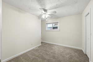 Unfurnished bedroom featuring a textured ceiling, carpet flooring, and a ceiling fan