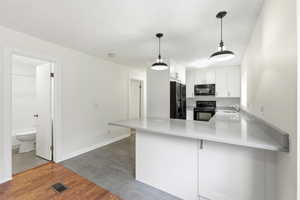 Kitchen with wood finish floors, white cabinets, black appliances, a peninsula, and a kitchen bar
