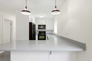 Kitchen with white cabinetry, black appliances, decorative light fixtures, a peninsula, and light stone countertops