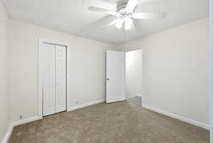 Unfurnished bedroom featuring carpet, a ceiling fan, a closet, and a textured ceiling
